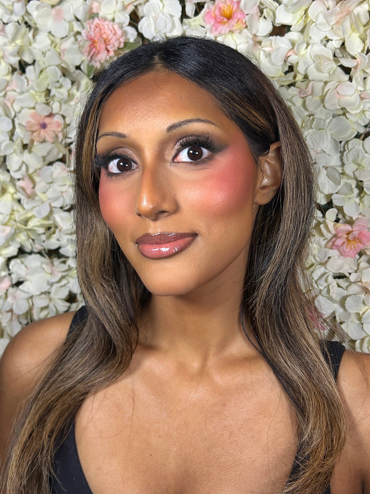 Full glam makeup with smoky eyes and glossy lips against a floral backdrop