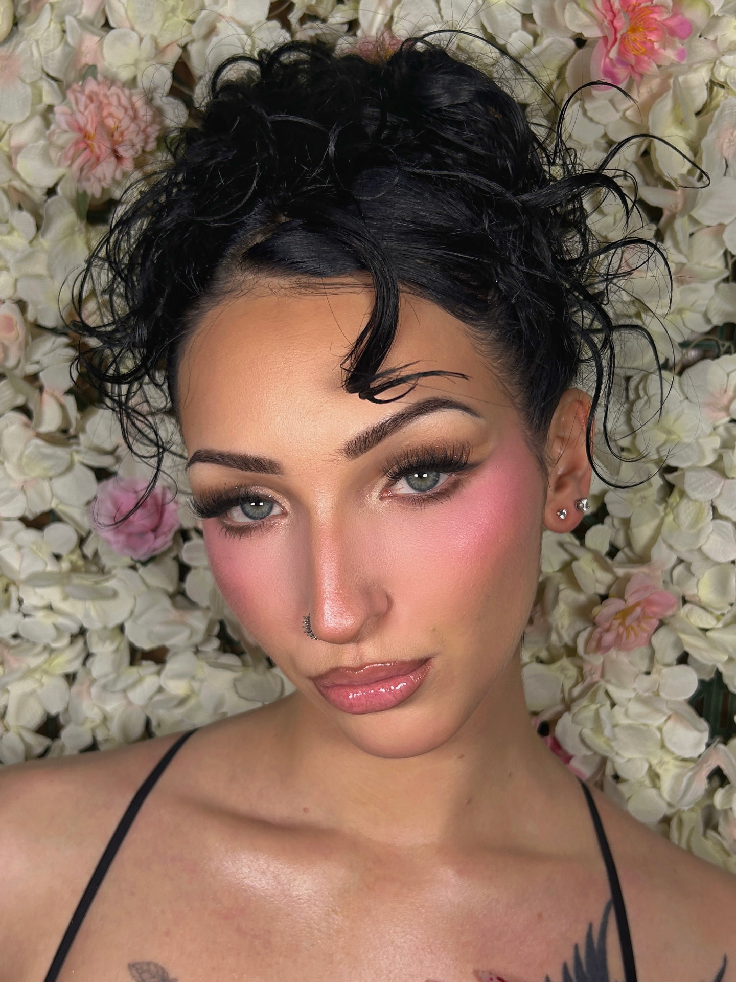 Full glam makeup with soft pink blush and glossy lips against a floral backdrop